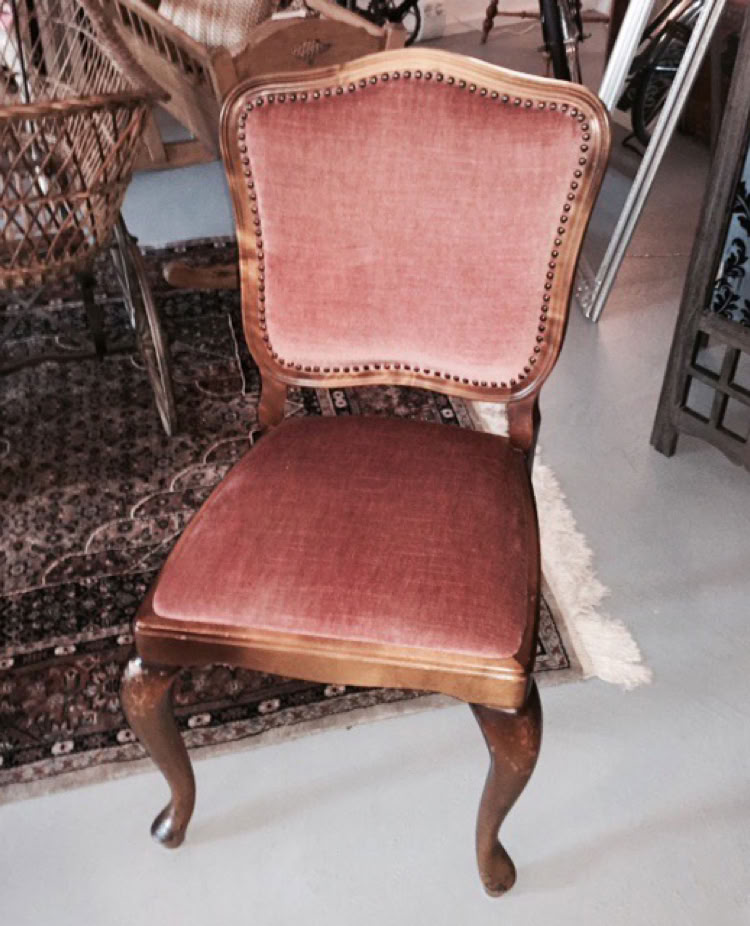 Ein antiker Stuhl mit rotem Polster und Holzrahmen steht auf einem gemusterten Teppich.