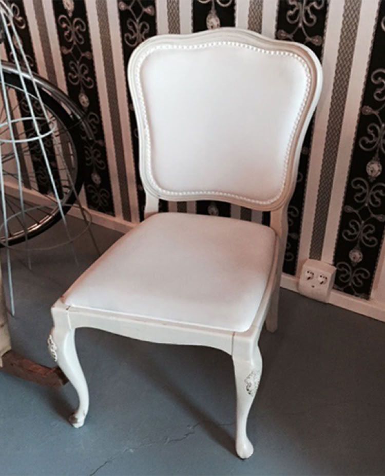 Ein weißer, gepolsterter Stuhl mit geschwungenen Beinen steht auf einem grauen Boden vor einer gestreiften Tapete.